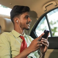 an indian man sitting in a car with his phone